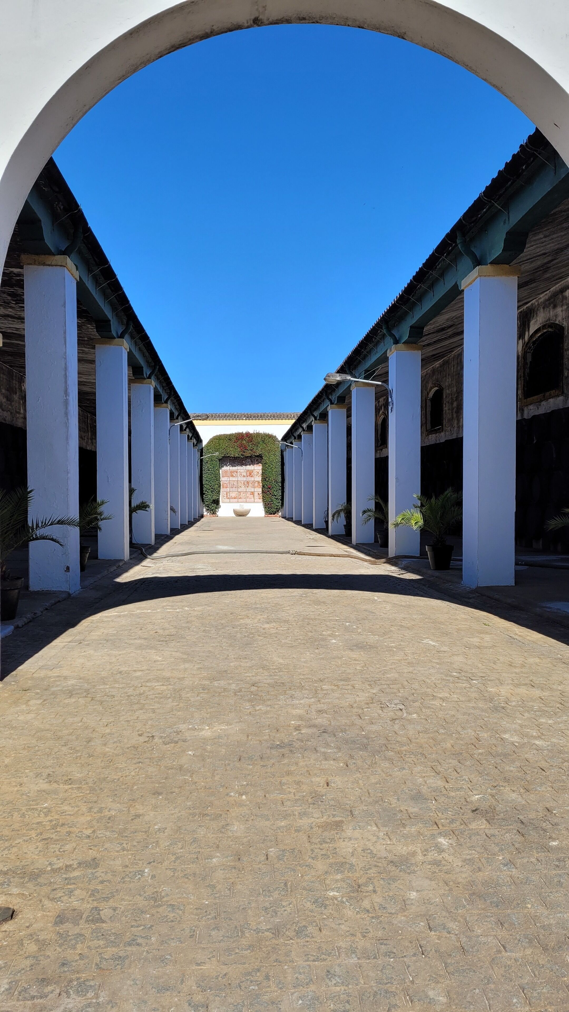 A corridor with white columns, a tiled floor, and a clear blue sky.