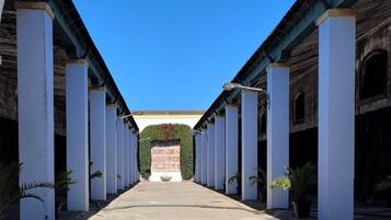 A corridor with white columns, a tiled floor, and a clear blue sky.