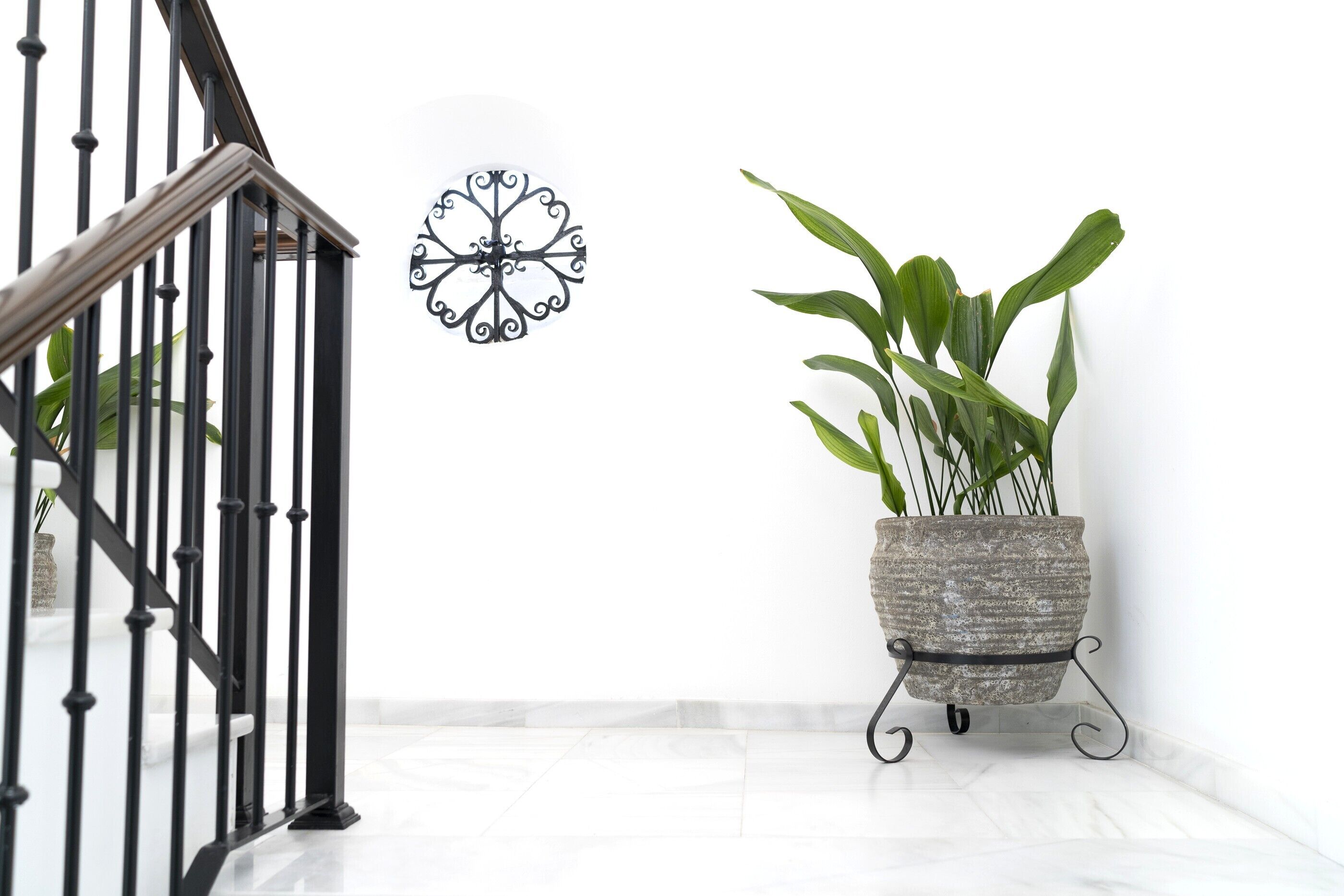 A staircase with black railings, a wall-mounted decorative metal piece, and a potted plant on a stand.