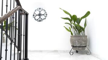 A staircase with black railings, a wall-mounted decorative metal piece, and a potted plant on a stand.
