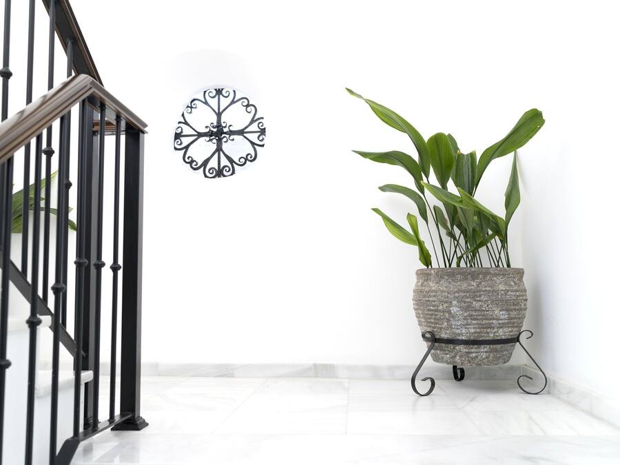 A staircase with black railings, a wall-mounted decorative metal piece, and a potted plant on a stand.