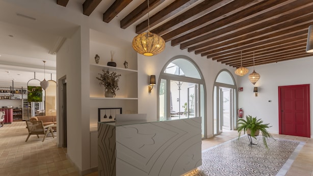 A modern hotel lobby with a reception desk, patterned floor, wooden ceiling beams, and a red door. - Albariza Hotel Boutique (Sanlucar de Barrameda)