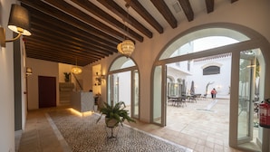 A spacious lobby with a patterned floor, wooden ceiling beams, and large arched glass doors leading to an outdoor patio area. - Albariza Hotel Boutique (Sanlucar de Barrameda)
