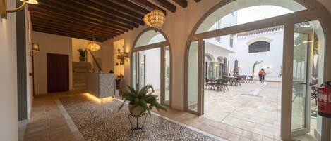 A spacious lobby with a patterned floor, wooden ceiling beams, and large arched glass doors leading to an outdoor patio area.