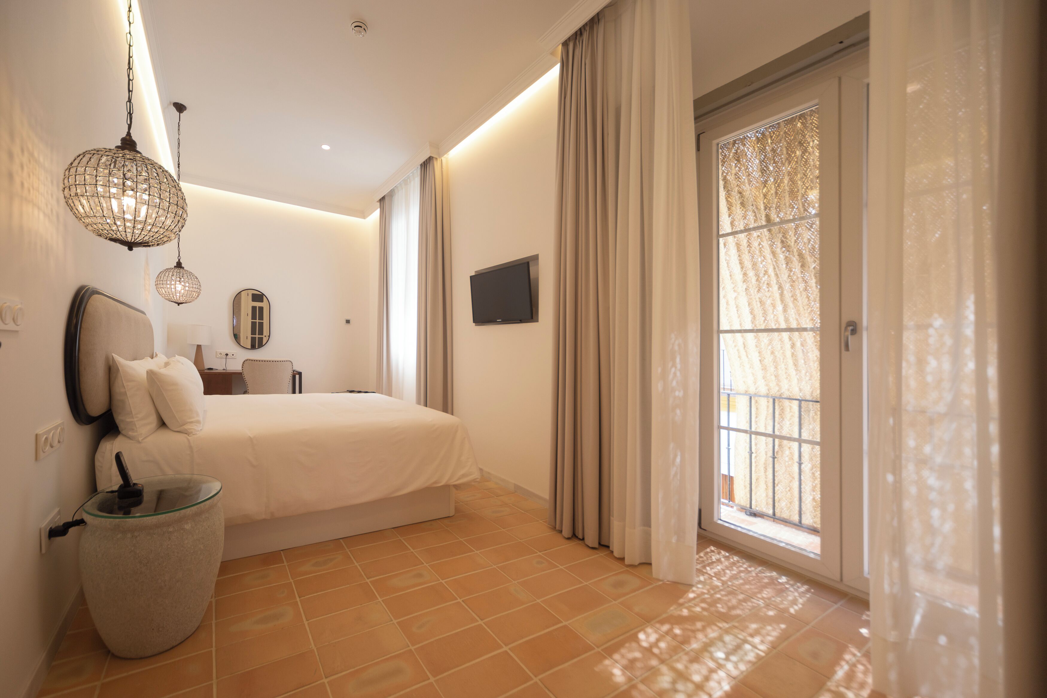 Habitación de hotel moderna con una cama grande, un televisor de pantalla plana, una mesita de noche, una lámpara y vistas al exterior a través de un amplio ventanal.