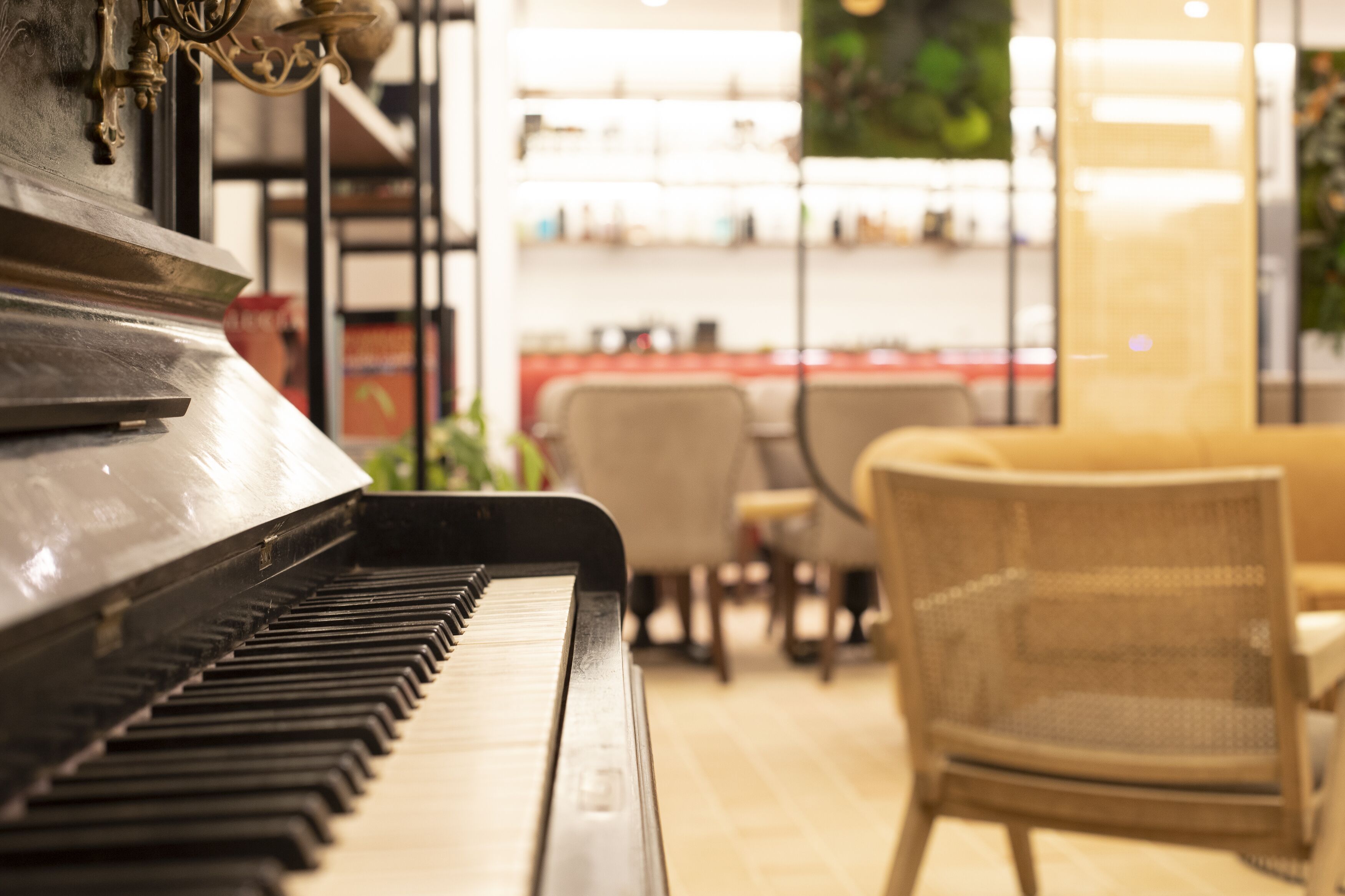A piano in a room with a sofa and chairs, and shelves with items in the background.