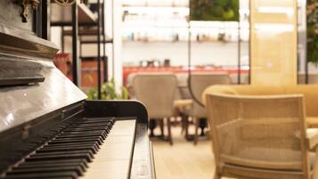 A piano in a room with a sofa and chairs, and shelves with items in the background.