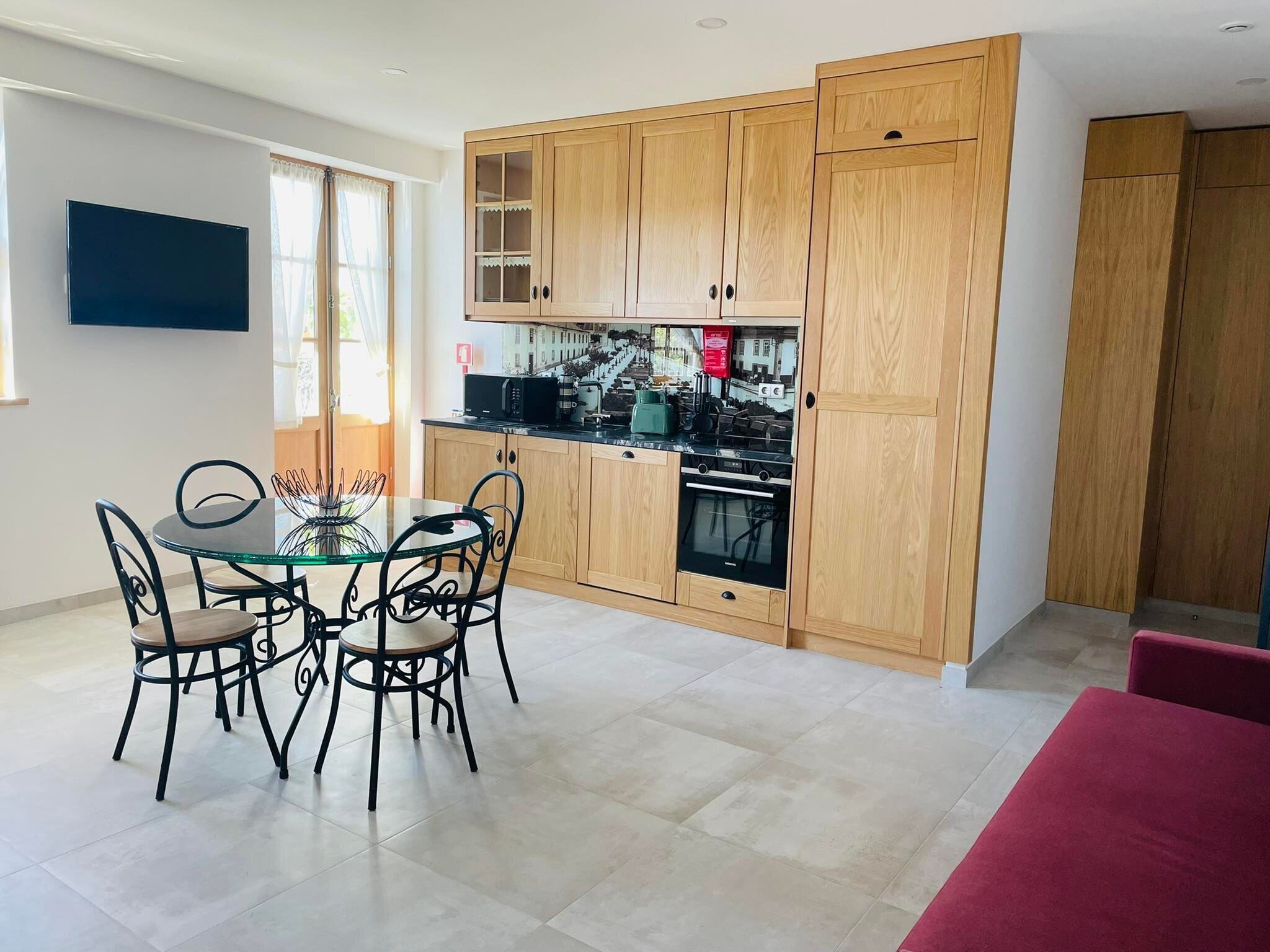 Een moderne keuken met houten kastjes, een eettafel met stoelen en een flatscreen televisie aan de muur.