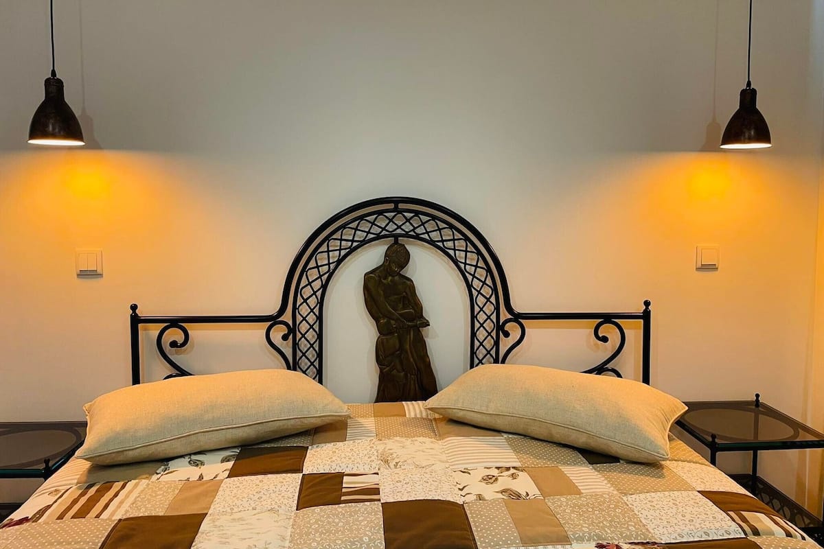 Una cama con un cabecero decorativo, dos mesitas de noche y dos lámparas de pared.