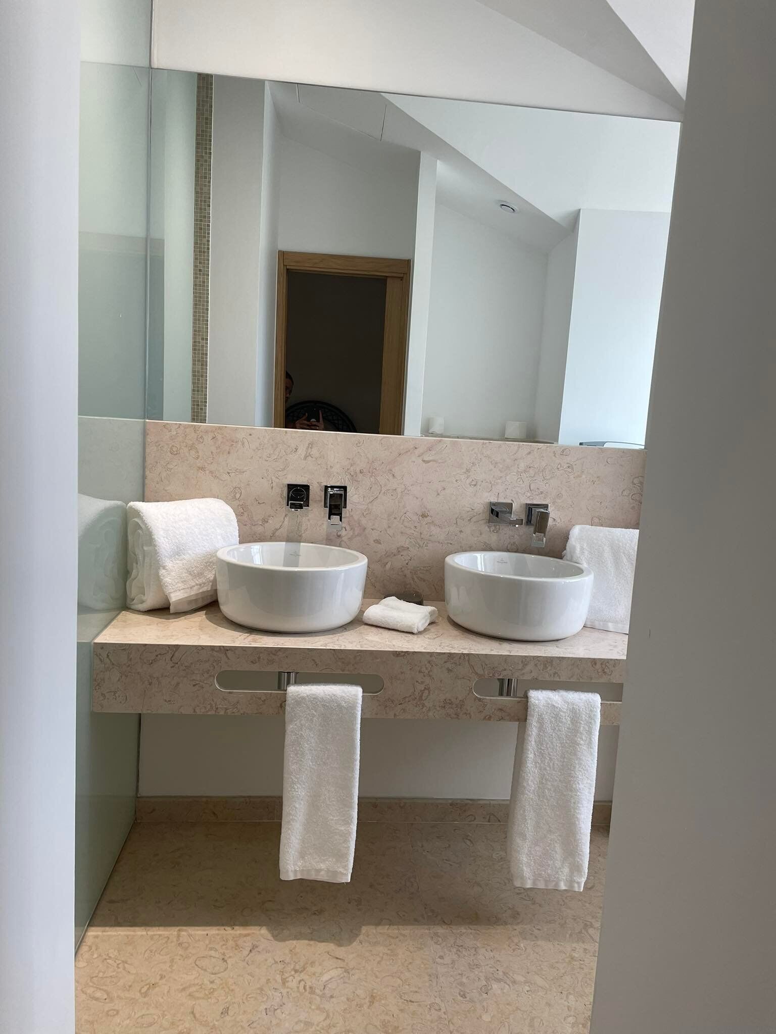 Um banheiro moderno com duas pias grandes brancas, um espelho e um porta-toalhas.