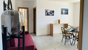 A modern living room with a red sofa, a glass coffee table, and a dining area with a small table and chairs. - Casa Guardião (Chaves)