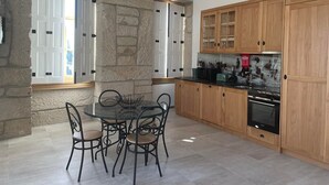 A modern kitchen with stone walls, wooden cabinets, and a round dining table with chairs. - Casa Guardião (Chaves)