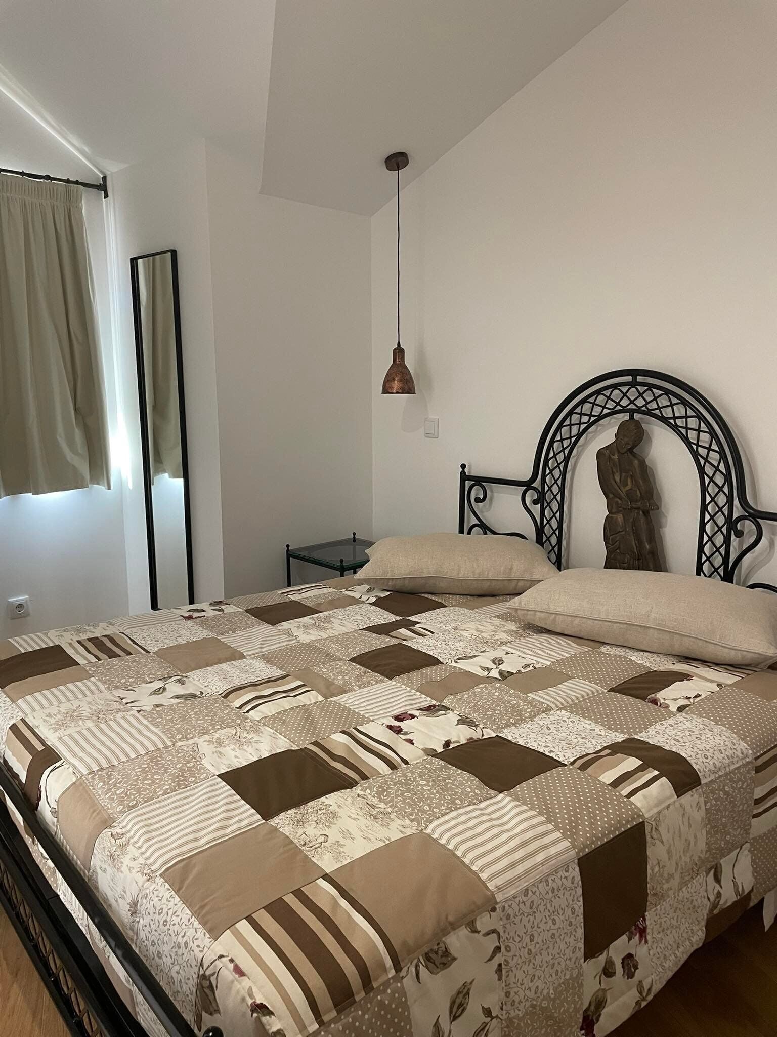 A bedroom with a bed, a nightstand, a wall-mounted lamp, and a statue.