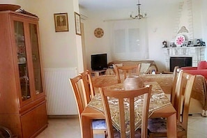 Uma sala de jantar com mesa e cadeiras de madeira, televisão e lareira.