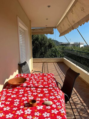 Uma varanda com uma mesa coberta por uma toalha de mesa florida vermelha, duas cadeiras, uma tigela e um pequeno vaso.