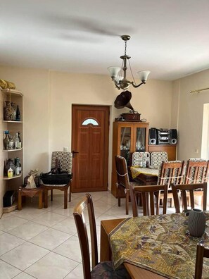 Uma sala de jantar com uma mesa de madeira, cadeiras, um candelabro e um armário com alto-falantes.