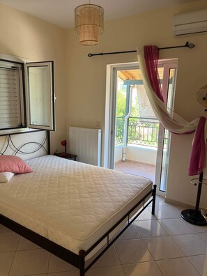 A bedroom with a bed, a window with blinds, a radiator, an air conditioning unit, and a balcony with a curtain.