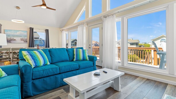 A spacious living room with a blue sofa, a white coffee table, and large windows offering a view of the neighborhood.