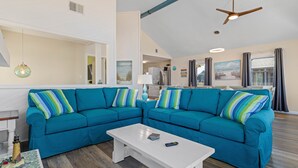 A living room with a teal sectional sofa, a white coffee table, and a ceiling fan.