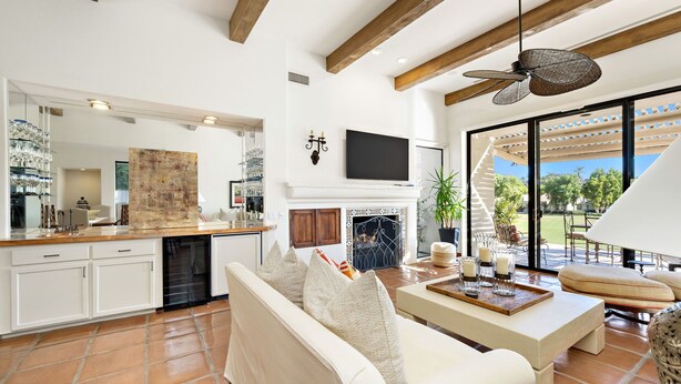 A spacious living area with a fireplace, a TV mounted above it, and a large window offering a view of the outdoors. - Los Estados #66 - 3 BD /3.5 BA, 2586sf (La Quinta)