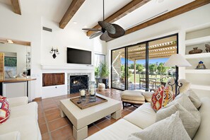 A spacious living room with a fireplace, comfortable seating, and a large window offering a view of the outdoors. - Los Estados #66 - 3 BD /3.5 BA, 2586sf (La Quinta)