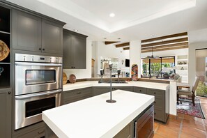 A modern kitchen with built-in appliances, a large island, and a view of the outdoors. - Los Estados #66 - 3 BD /3.5 BA, 2586sf (La Quinta)