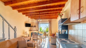 A cozy interior with a wooden ceiling, a kitchen with a stove, a dining area with chairs, and a sofa. - Holiday Home "Balis Panorama" with Sea View, Balcony, Garden & Wi-Fi (Corfu)