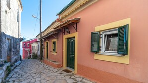 A narrow cobblestone street with buildings painted in pastel colors, featuring traditional architecture and a small entrance with a door and window. - Holiday Home "Balis Panorama" with Sea View, Balcony, Garden & Wi-Fi (Corfu)