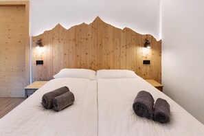 Un lit double avec deux serviettes enroulées, un lambris en bois sur les murs et deux tables de chevet fixées au mur.
