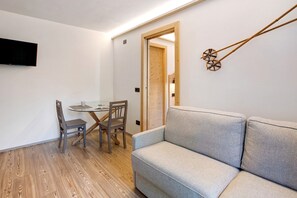Un salon moderne avec un canapé gris, un plancher en bois, une table à manger avec des chaises et un téléviseur à écran plat fixé au mur.
