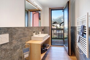 A modern bathroom with a sink, towel rack, and a view of mountains through the door.