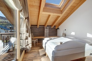 Une chambre avec une lucarne, des poutres en bois, un lit, un bureau et une vue sur l’extérieur.