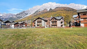 A row of chalet-style buildings with wooden exteriors and balconies, set against a backdrop of snow-capped mountains and a clear blue sky. - Apartment "Baita Emilia e Daniele 13" with Mountain View, Balconies and Wi-Fi (Bormio)