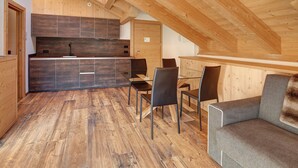 A modern kitchen with dark wooden cabinets and a dining area with a gray sofa and black chairs. - Apartment "Baita Emilia e Daniele 13" with Mountain View, Balconies and Wi-Fi (Bormio)
