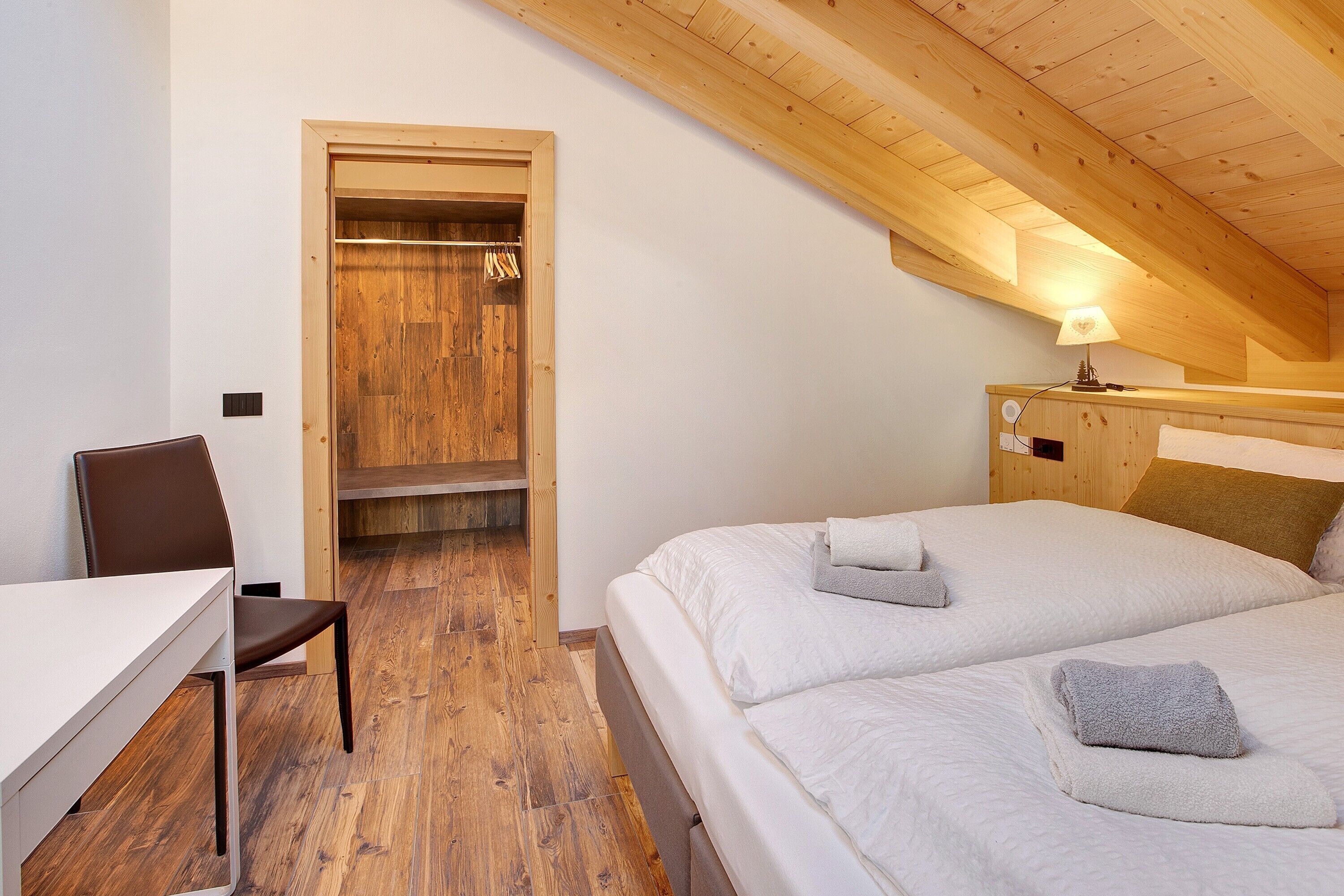Un dormitorio con techo de madera, una cama con ropa de cama blanca, una mesita de noche con lámpara y un armario de madera.
