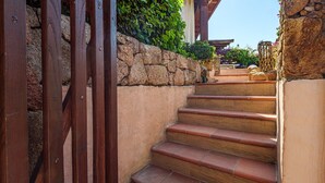 Unos escalones de madera conducen a un muro de piedra, con una puerta de madera a la izquierda.