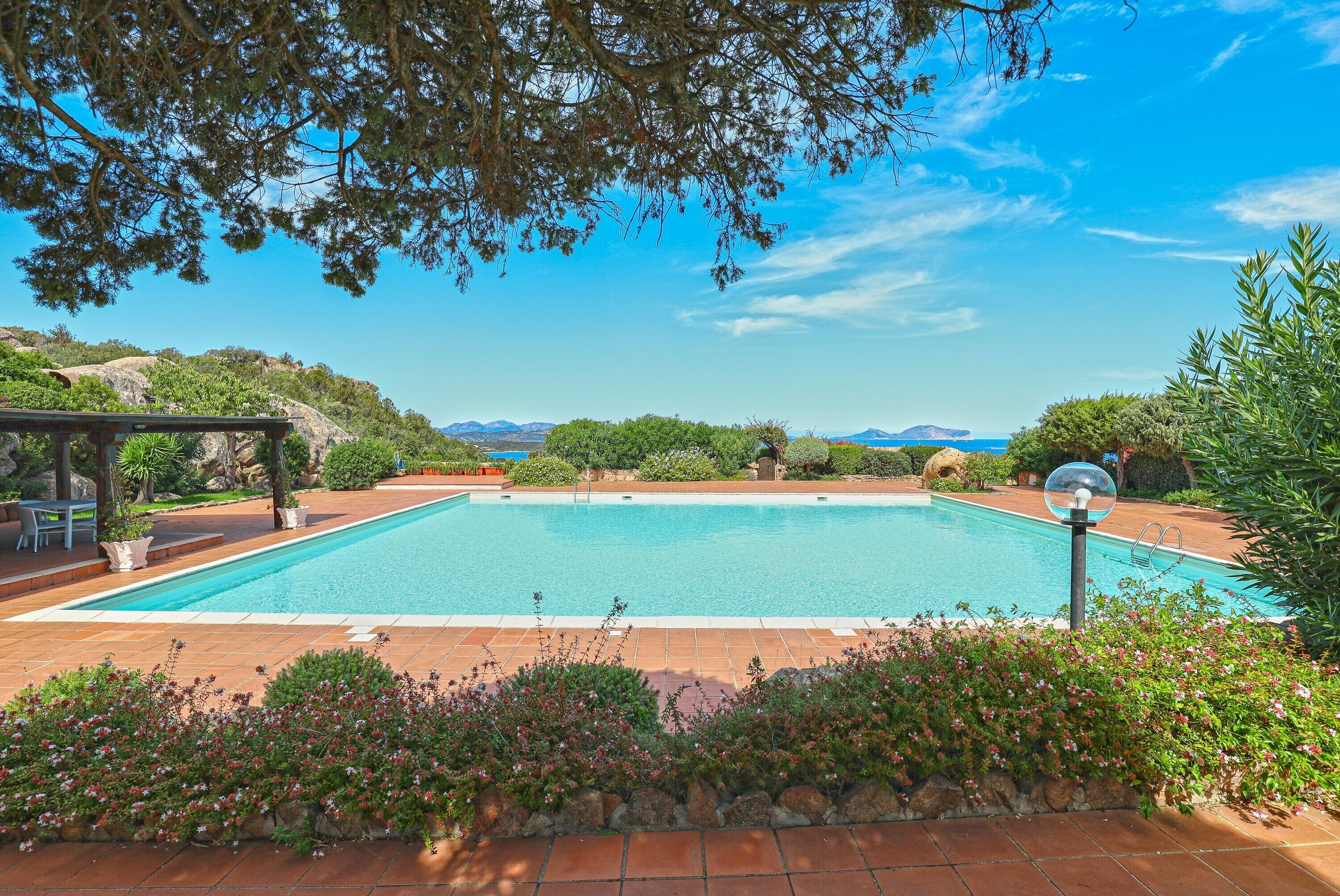 A rectangular swimming pool with a clear blue water surface, surrounded by a tiled deck and a stone wall.