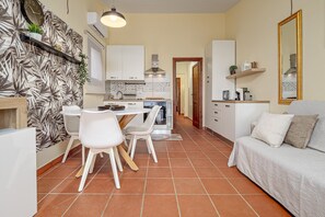 Une cuisine moderne avec des meubles blancs, un coin repas avec des chaises blanches et un salon avec un canapé.