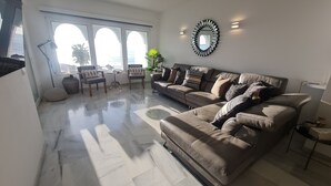 A modern living room with a large sofa, a coffee table, and a dining area with chairs. There is a large window with a view of the outdoors. - Apartment "240 Front Line Beach La Cala" with Wi-Fi (la cala de mijas)