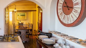 Un comedor con un gran reloj de pared, una cocina con estufa y una mesa de comedor con platos y tazas.