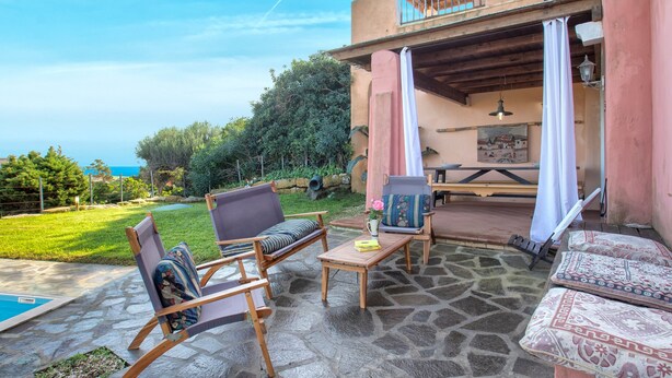 Un patio exterior con suelo de piedra, mobiliario de madera y vista al mar.