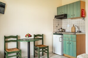 A compact kitchen with a dining table, two chairs, a refrigerator, and a stove.