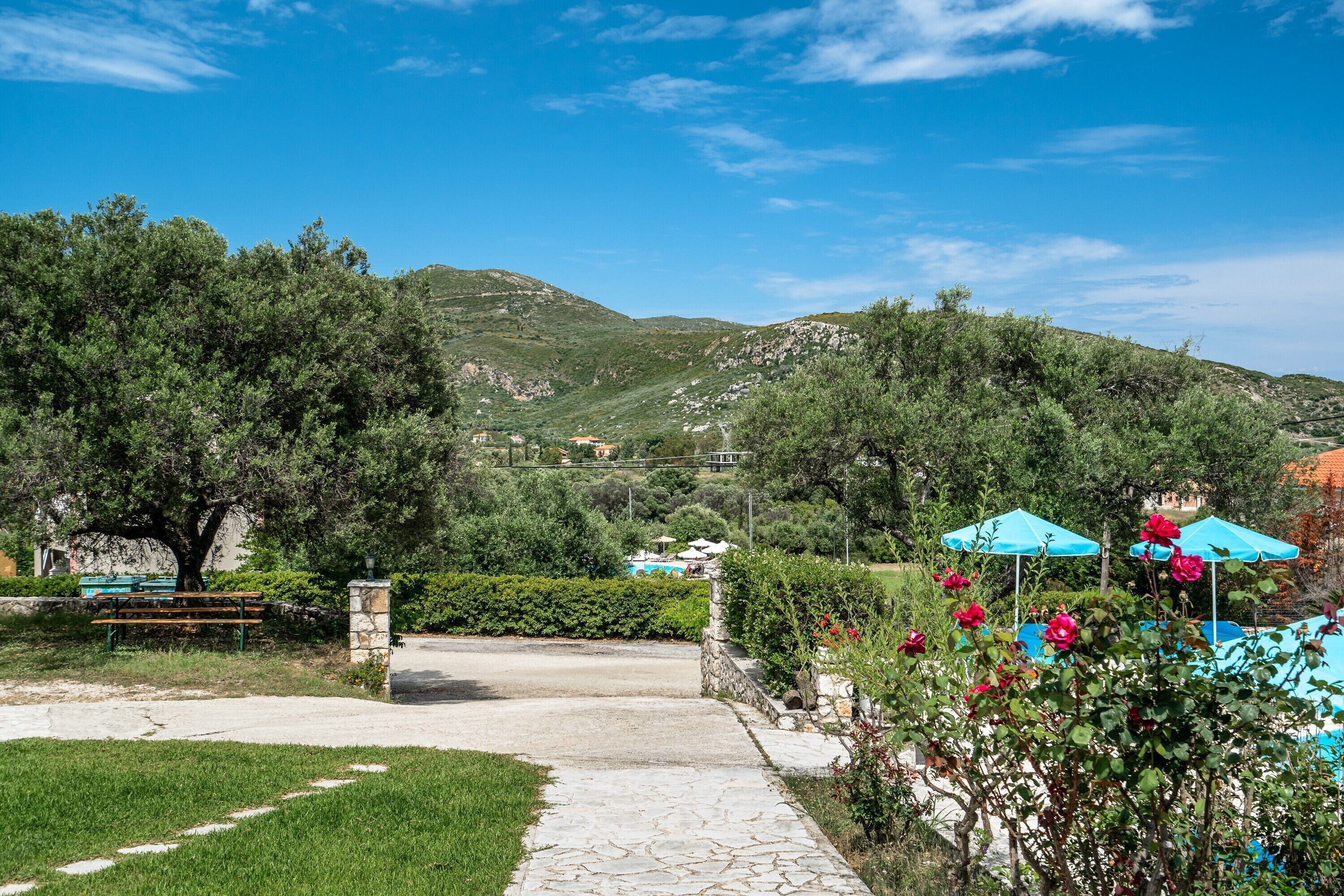 Un chemin pavé mène à un banc et à un mur de pierre, le tout étant entouré d’une végétation luxuriante et ayant une chaîne de montagnes en toile de fond.