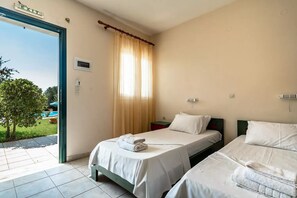 Une chambre d’hôtel avec deux lits, une fenêtre avec des rideaux, un panneau de signalisation indiquant la sortie, et une vue sur une piscine à l’extérieur.