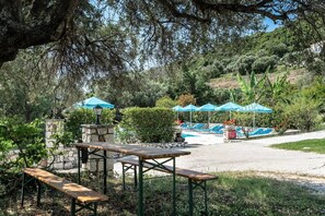 Ein Poolbereich mit blauen Sonnenschirmen, einer Steinmauer und einem Picknicktisch.