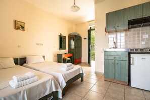 Una habitación con dos camas, un pequeño espacio de cocina y una puerta que da al exterior.