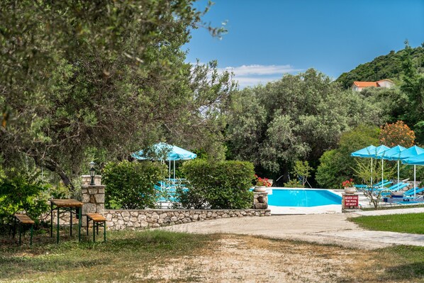 Un área de piscina con un muro de piedra, sombrillas azules y sillas de descanso.