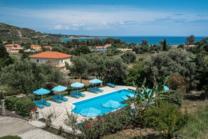 Zona de piscina con sillones de descanso y sombrillas, rodeada de vegetación y con vistas al paisaje costero.