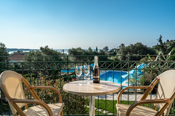 A balcony with wicker chairs, a table with a bottle and glasses, and a pool in the background.