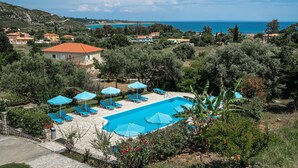 A pool area with lounge chairs and umbrellas, surrounded by greenery and overlooking a coastal landscape. - Studio Apartment "Anemona 3" with Shared Pool & Wi-Fi (kefalonia)